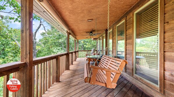 A wooden porch with a swing chair, a table, and a sign indicating 'Spring River Fishing Cabins'.