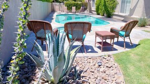 Un jardin avec une piscine, entouré de fauteuils en osier et d’une grande plante d’agave.