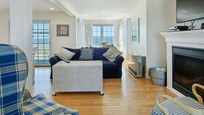 A spacious living room with a dark blue sofa, a white ottoman, and a fireplace. - STUNNING BEACHSIDE HOME-WELLS BEACH: 180 DEGREE OCEAN VIEWS: 9-1 to 9-3 open (Wells)