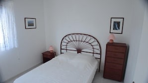 A bedroom with a single bed, a dresser, two bedside tables, and two framed pictures on the walls.