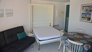 A compact room with a bed, a sofa, a small table, and a chair.