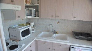A compact kitchen with a microwave, coffee maker, sink, and a small stove.