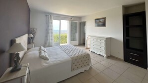 Un dormitorio con cama, cómoda, cuadro y vistas al exterior.