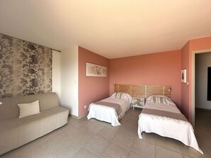 Ein Zimmer mit einer Couch, zwei Betten mit Holz-Kopfteilen, floralem Wandpapier und einem Bild an der Wand.