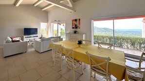 Un salón amplio con una mesa de comedor, sillas blancas, un sofá y un televisor.