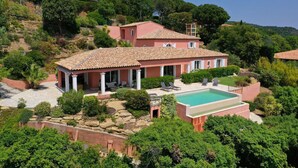 Una casa grande con piscina, rodeada de abundante vegetación y colinas.