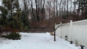 Een sneeuwbedekte achtertuin met een witte hek, een boom en een lantaarn.