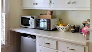 Een kleine keuken met witte kastjes, een magnetron, een broodrooster en een fruitmand.