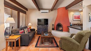 A cozy living room with a fireplace, a sofa, a coffee table, and a television. - Fort Marcy 68 | Walk to Plaza | Kiva Fireplace | Full Kitchen | Hot Tub | Pool | Single Level (Santa Fe)