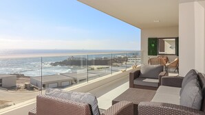 Ein Balkon mit Korbmöbeln, Blick auf den Ozean und einer grünen Wand.