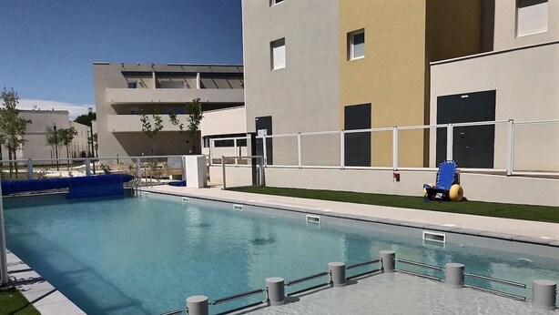 A swimming pool with a modern building in the background. - Appartement Confortable Près de la Plage (Sérignan)