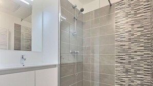 A modern bathroom with a glass-enclosed shower, a white sink, and a tiled wall with a unique pattern. - Appartement Confortable Près de la Plage (Sérignan)