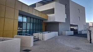 A modern building with a flat roof, large windows, and a courtyard with planters. - Appartement Confortable Près de la Plage (Sérignan)