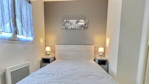 Un dormitorio con una cama grande, dos mesitas de noche con lámparas, una obra de arte en la pared y una ventana con cortinas.