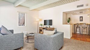 Una sala de estar con dos sofás grises, una mesa de centro, un televisor y un pequeño comedor con dos sillas.
