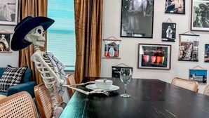 Ein Essbereich mit einer Skeletfigur, einem Tisch mit einer weißen Schüssel und einem Weinglas, sowie verschiedenen gerahmten Bildern an den Wänden.