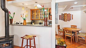 A kitchen with a wood-burning stove, wooden cabinets, and a dining area with a table and chairs. - Fort Marcy 78 | Walk to Plaza | Wood Fireplace | Full Kitchen | Hot Tub | Pool | Single Level (Santa Fe)