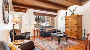 A living room with a sofa, a coffee table, a cabinet, and a lamp. - Fort Marcy 78 | Walk to Plaza | Wood Fireplace | Full Kitchen | Hot Tub | Pool | Single Level (Santa Fe)