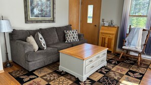 A living room with a grey sofa, a wooden coffee table, a patterned rug, and a framed picture on the wall.