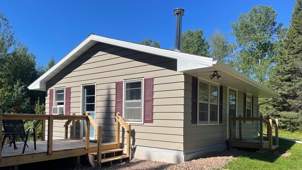 A small cabin with a porch, a chimney, and a gravel driveway.