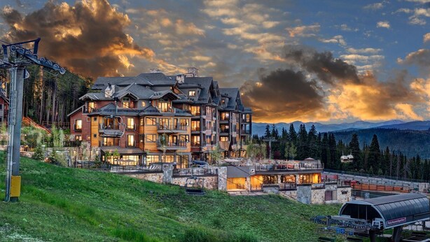 A multi-story lodge with a ski lift, surrounded by mountains and a cloudy sky.