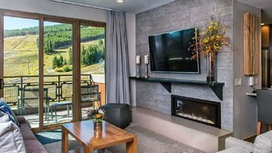A modern living room with a fireplace, a flat-screen TV, and a large window overlooking a scenic landscape.