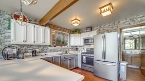 A kitchen with white cabinets, a stainless steel refrigerator, a microwave, and a stove. There is a brick wall and wooden beams on the ceiling. - Deck & Scenic Views: Munds Park A-Frame Cabin (Munds Park)
