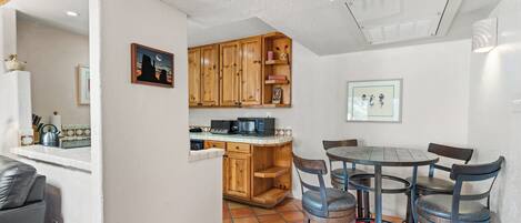 A compact kitchen with wooden cabinets, a dining table with chairs, and a red rug.