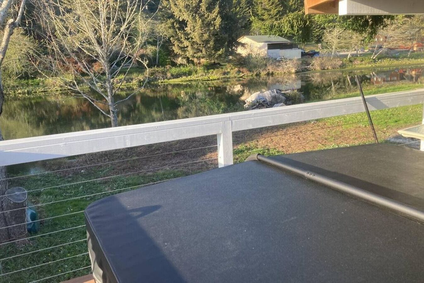 A view from a balcony overlooking a lake with a wooden deck and a white railing.
