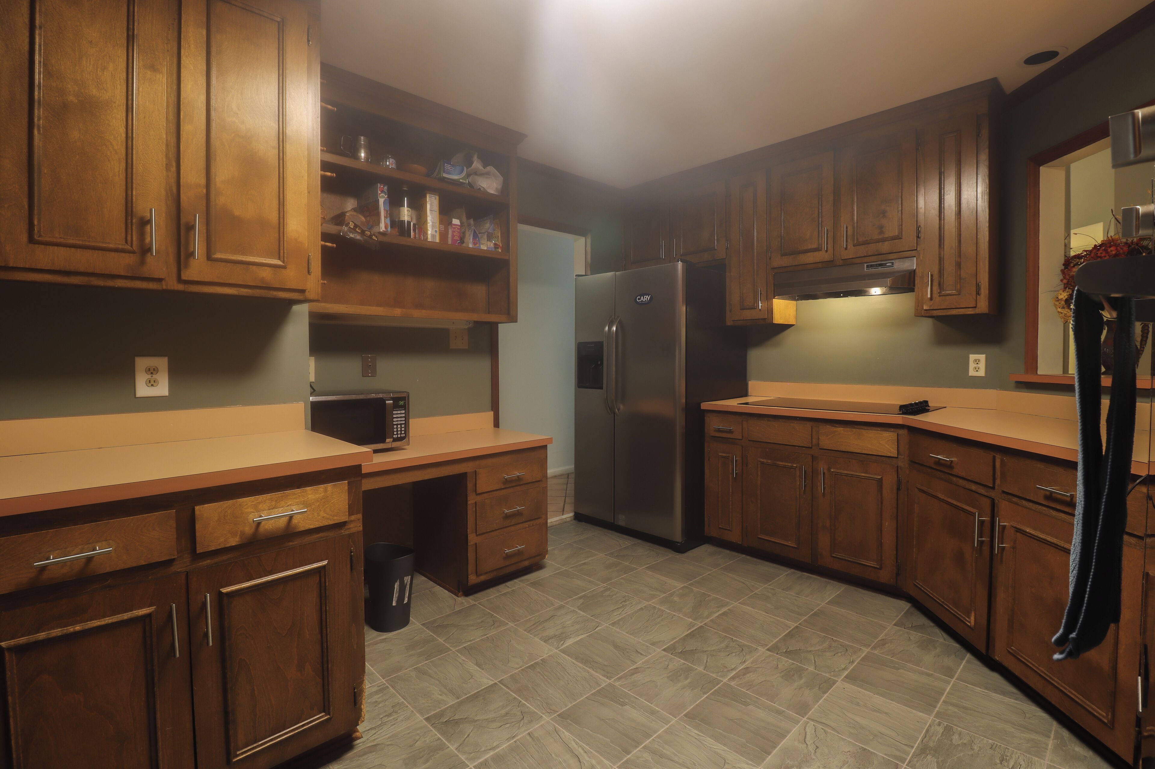 A kitchen with wooden cabinets, a stainless steel refrigerator, a microwave, and a trash can.