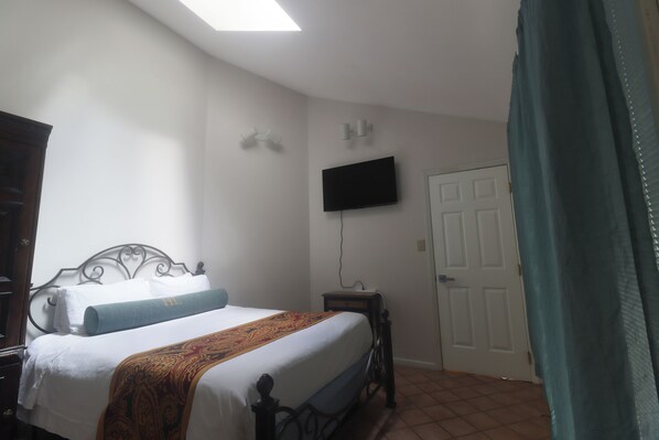 A bedroom with a bed, a television mounted on the wall, a door, and a window with a curtain.