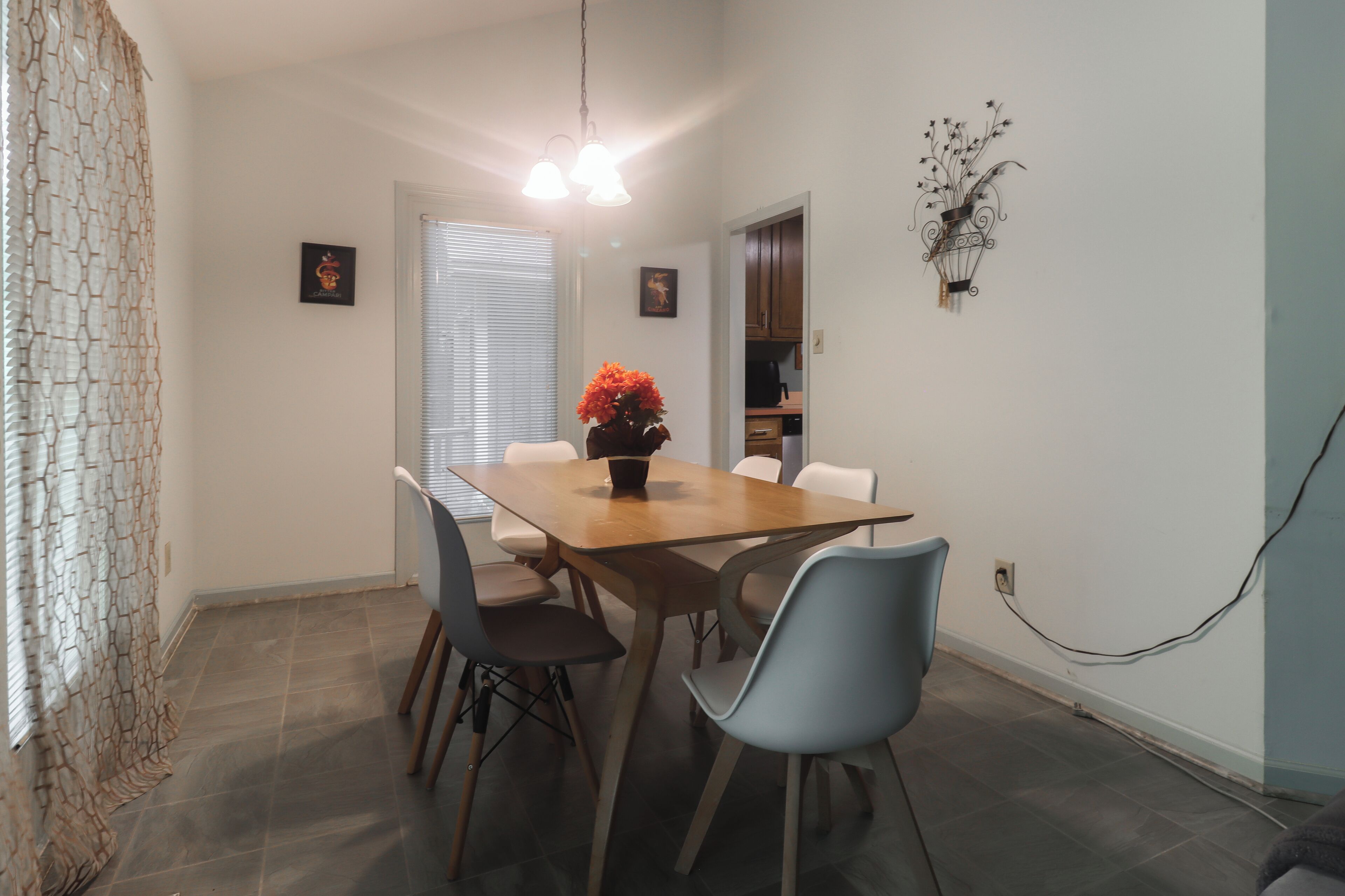 A dining area with a wooden table, four chairs, a vase with flowers, and a wall-mounted light fixture.