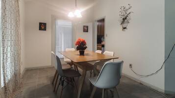 A dining area with a wooden table, four chairs, a vase with flowers, and a wall-mounted light fixture.