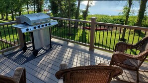Een terras met een barbecue, rieten stoelen en uitzicht op een meer.