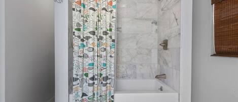 A shower with a patterned curtain, a bathtub, and a tiled floor.
