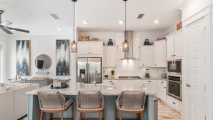A modern kitchen with white cabinets, a central island with bar stools, stainless steel appliances, and pendant lighting. - 30A Top Rated! Free Golf Cart+Bikes+2 Pools+Bunks (Inlet Beach)