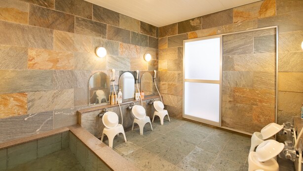 Un baño con paredes de piedra, un espejo grande y una bañera con una pequeña zona de estar.