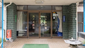 Entrada de hotel con suelo de baldosas, felpudo verde y farol de piedra.