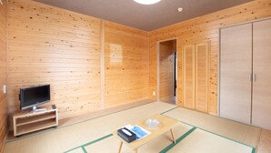Una habitación con paredes de madera, un televisor sobre un mueble bajo, una mesita con un libro y un cenicero, y un armario.