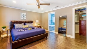 Une chambre avec un grand lit, un ventilateur de plafond, une table de chevet avec une lampe et une vue sur un balcon.