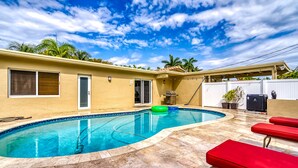 Un jardin avec une piscine, des chaises longues rouges et un espace patio couvert.