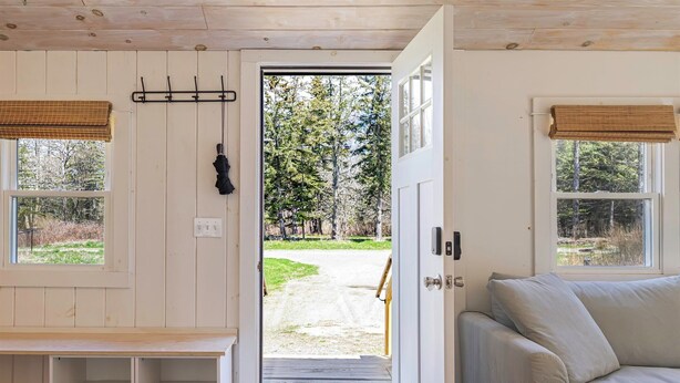 A wooden interior with a door leading to a forested area, a bench, and a sofa. - Romantic Forest Cabin - private, near everything (Bar Harbor)