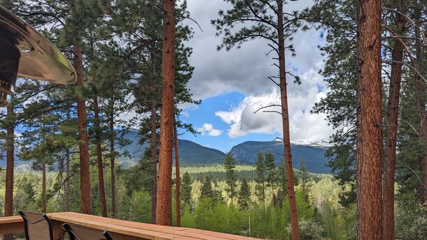 Eine Holzterrasse mit Stühlen mit Blick auf einen Wald und Berge.