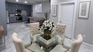 Un comedor moderno con una mesa de vidrio, sillas acolchadas y un jarrón de flores.