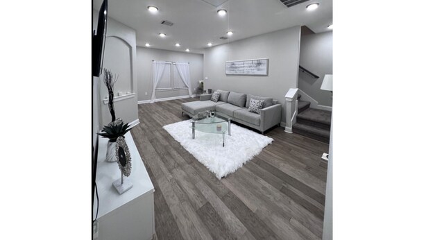 Una sala de estar moderna con un sofá gris, un tapete blanco y un televisor de pantalla plana montado en la pared.