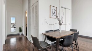 Un comedor con una mesa de madera y sillas negras, un jarrón con ramas y una obra de arte abstracta enmarcada en la pared.