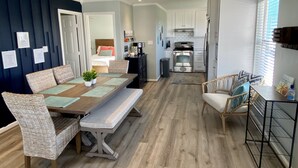 Una cocina moderna con armarios blancos, electrodomésticos de acero inoxidable y un comedor con mesa de madera y sillas de mimbre.