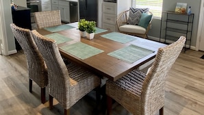 Una cocina moderna con alacenas blancas, un refrigerador de acero inoxidable y un comedor con sillas de mimbre y una mesa de madera.