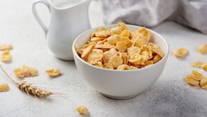 A bowl of cornflakes with a white mug in the background on a textured surface. - Blue Gums Hotel (Fairview Park)