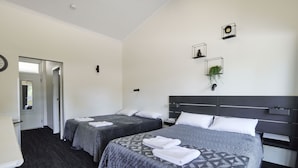 A hotel room with two beds, a dark wood floor, a white door, and a small plant on the wall. - Blue Gums Hotel (Fairview Park)